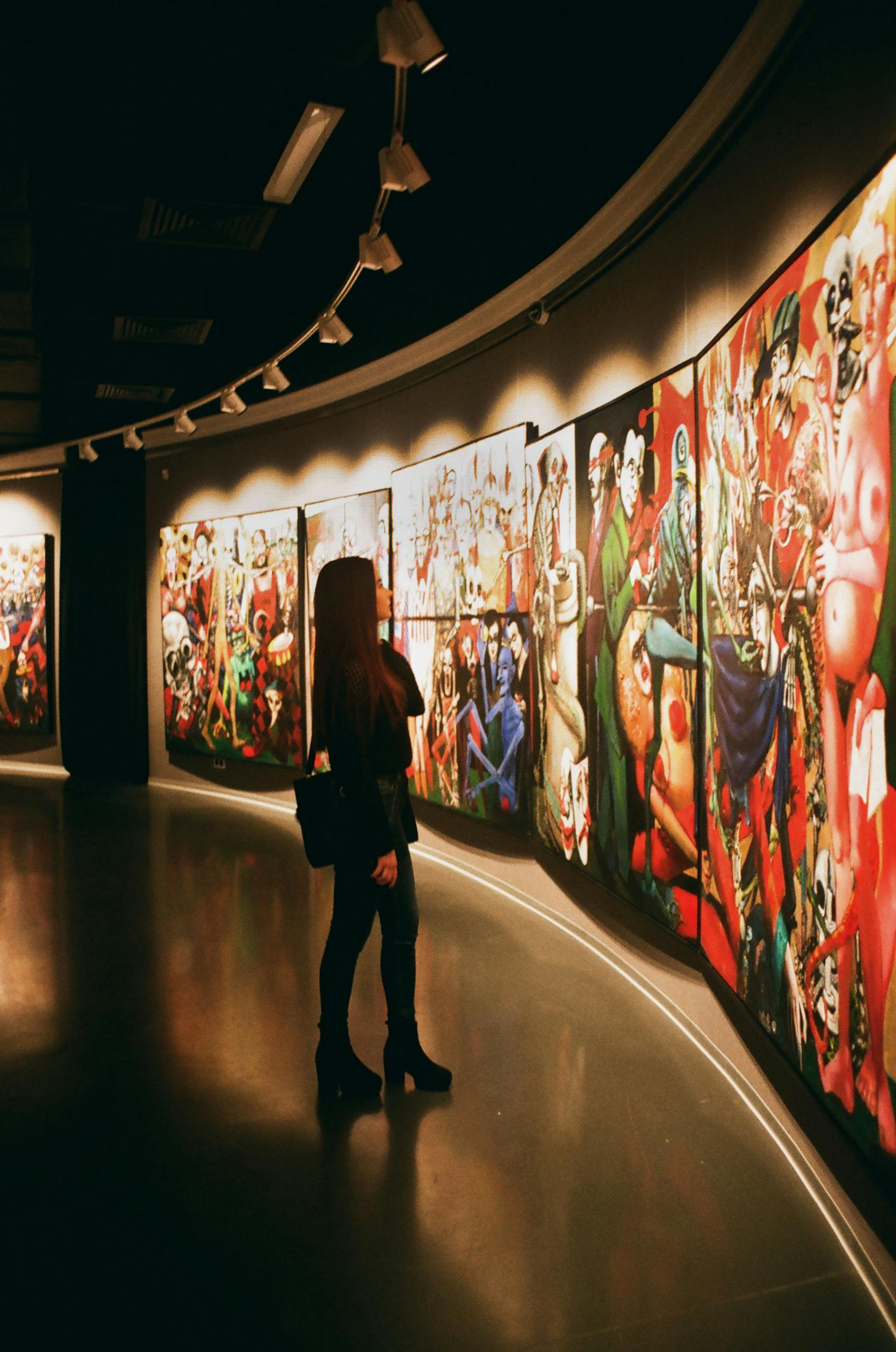 A woman observes vibrant paintings in an art gallery exhibition.